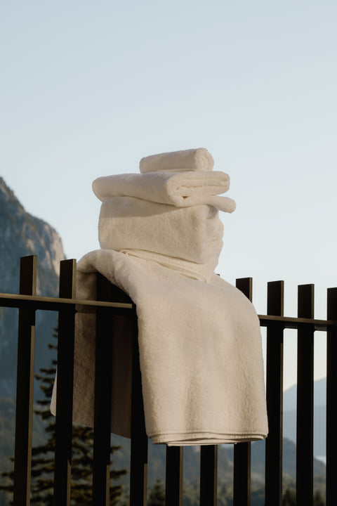 White bath towels on an iron fence overlooking mountains and trees. Towels by Takasa