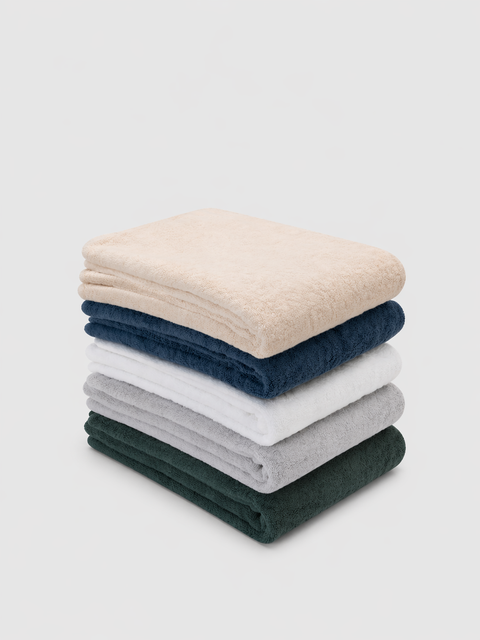 Stack of folded towels in natural, alps, white, mist and grove green on a light gray background
