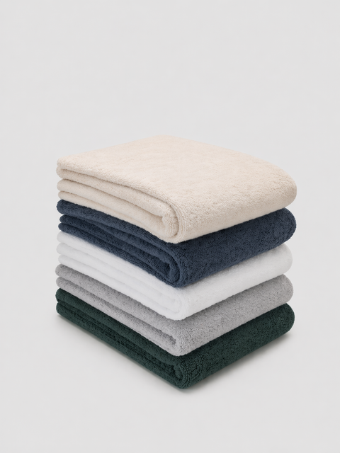 Stack of folded towels in natural, alps, white, green and light grey on a light gray background
